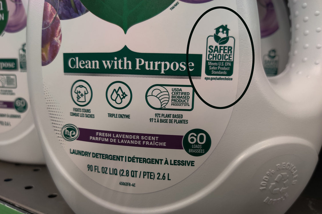 The bottom half of a white bottle of clothing detergent, the bottle shows a logo for EPA Safer Choice certification for a safer cleaning option