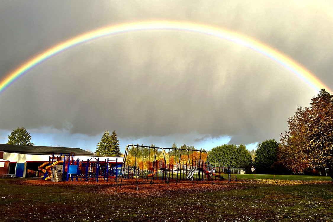 A full, brightly colored rainbow stretches over school playground.