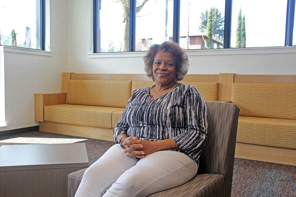 Portrait of an elder woman with short hair and a striped blouse smiling, sitting in a lounge area