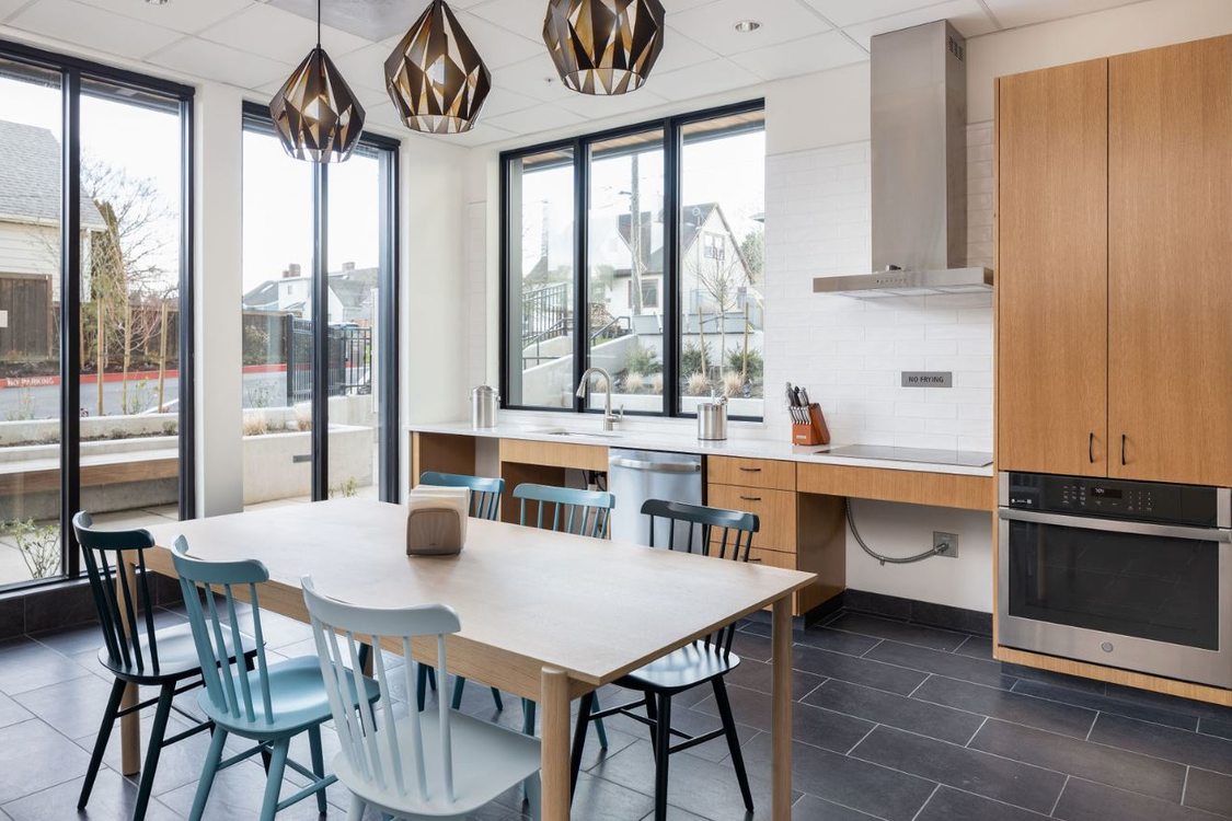 Communal kitchen with table, tall windows and glass doors, and hanging decorative lighting fixtures