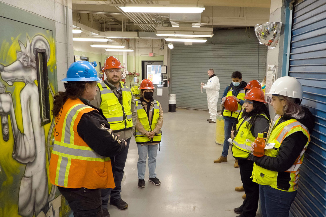 Group in safety vests and hardhats stand in a hallway of a hazardous waste disposal facility