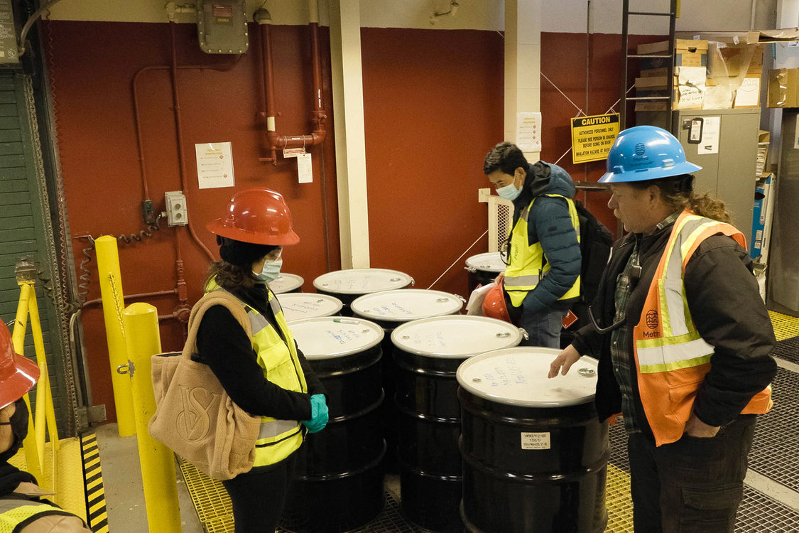 People in hardhats and safety vests look over 55 gallon drums filled with hazardous materials