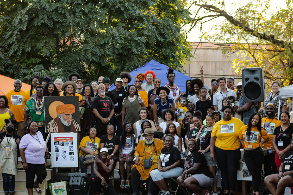 A crowd of mostly Black and brown people of all ages pose for a group photo at the Afro-topia pop-up event on stage.