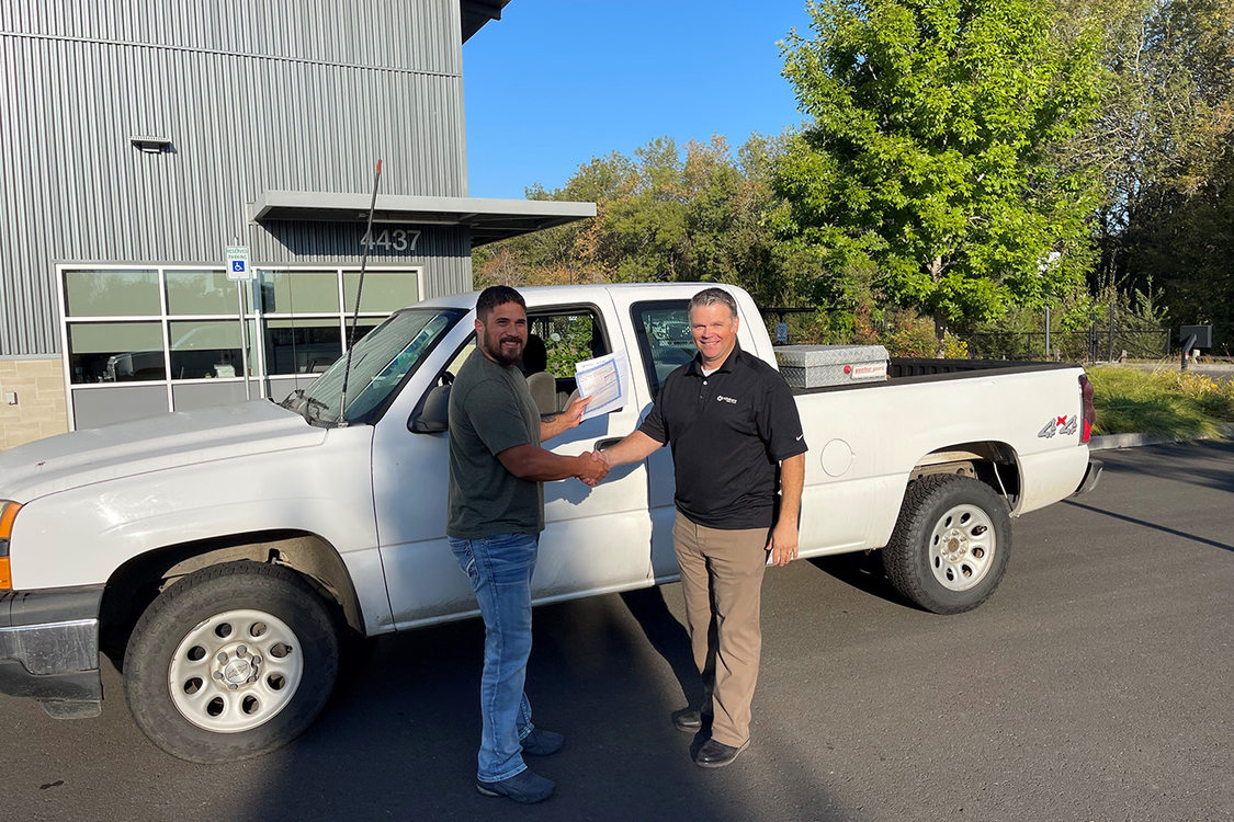 Two men shake hands in front of a white pickup truck