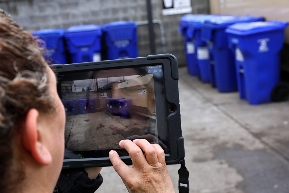 A woman documents the garbage and recycling bins at an apartment complex