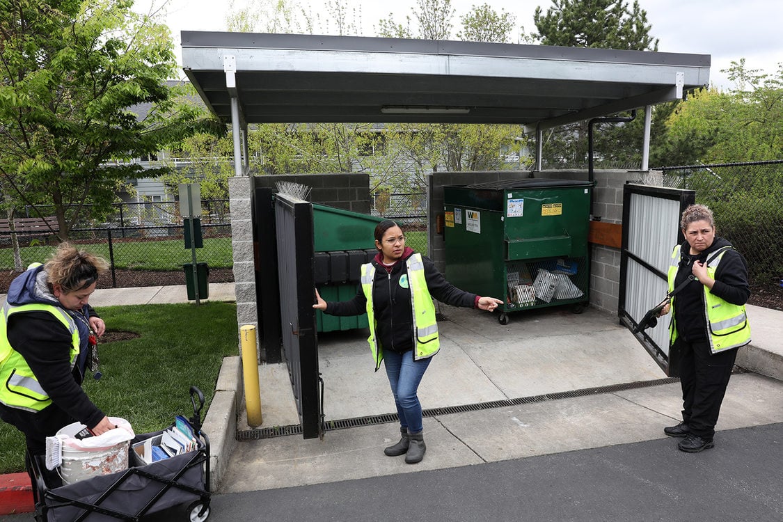 Three women in safety vests open the gates to a recycling and trash area at an apartment complex