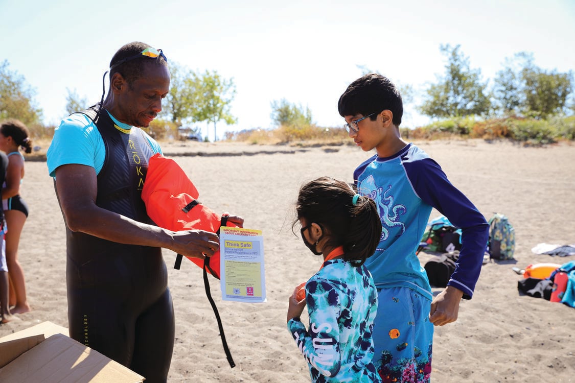 A swimming instructor shows two young children how to use a life vest 