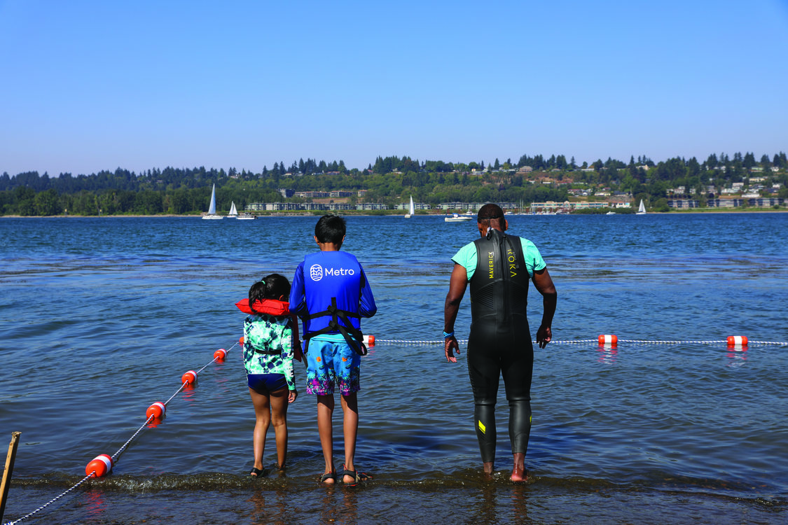 A swimming instructor shows two young children how to safely enter a river.