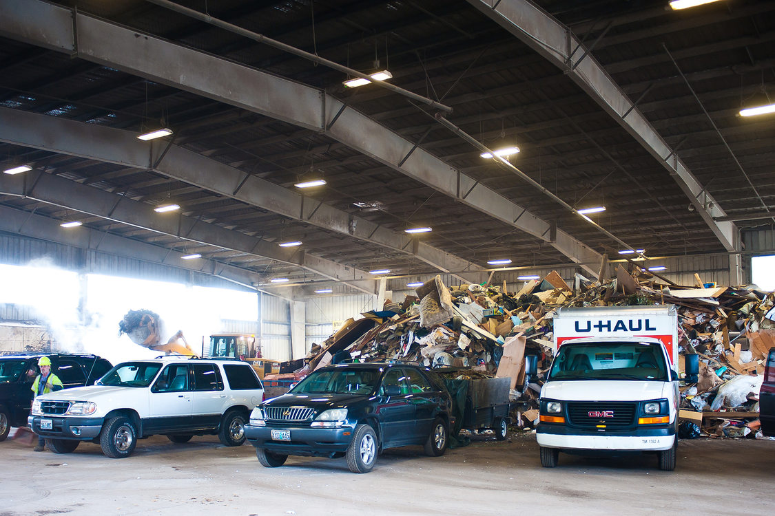 Five vehicles line up in front of a large pile of trash on the Metro South transfer station floor