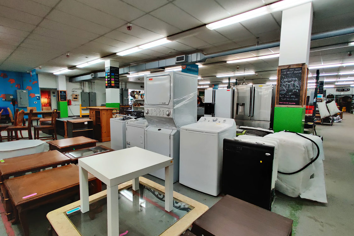 Inside of warehouse with tables in front and washers and dryers in a row behind it.