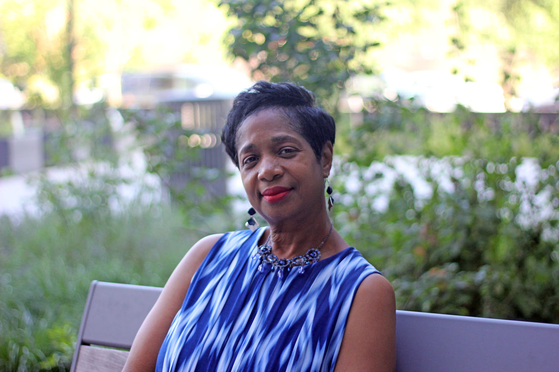 Woman with short dark hair and a blue print dress sitting at a bench