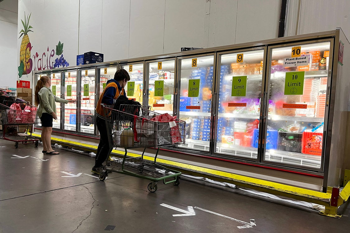 Two people stand in front of a 10-door freezer looking at food at a food bank