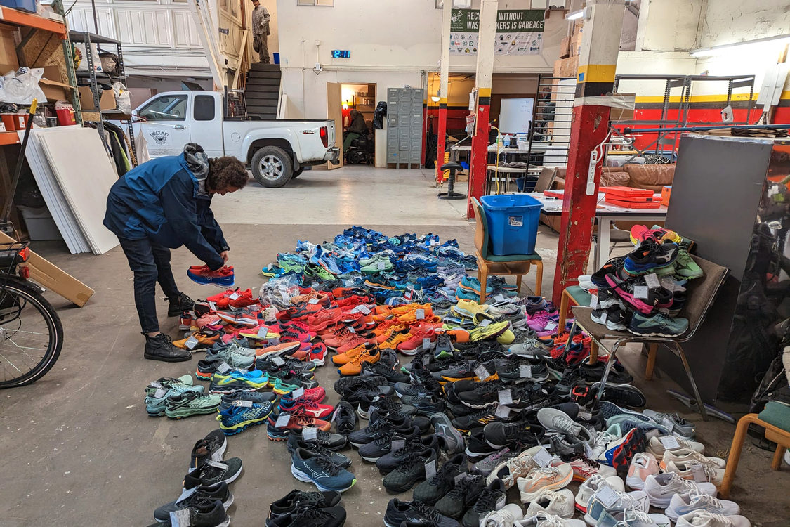 A person stands in front of a pile of shoes sorted by color on a warehouse floor