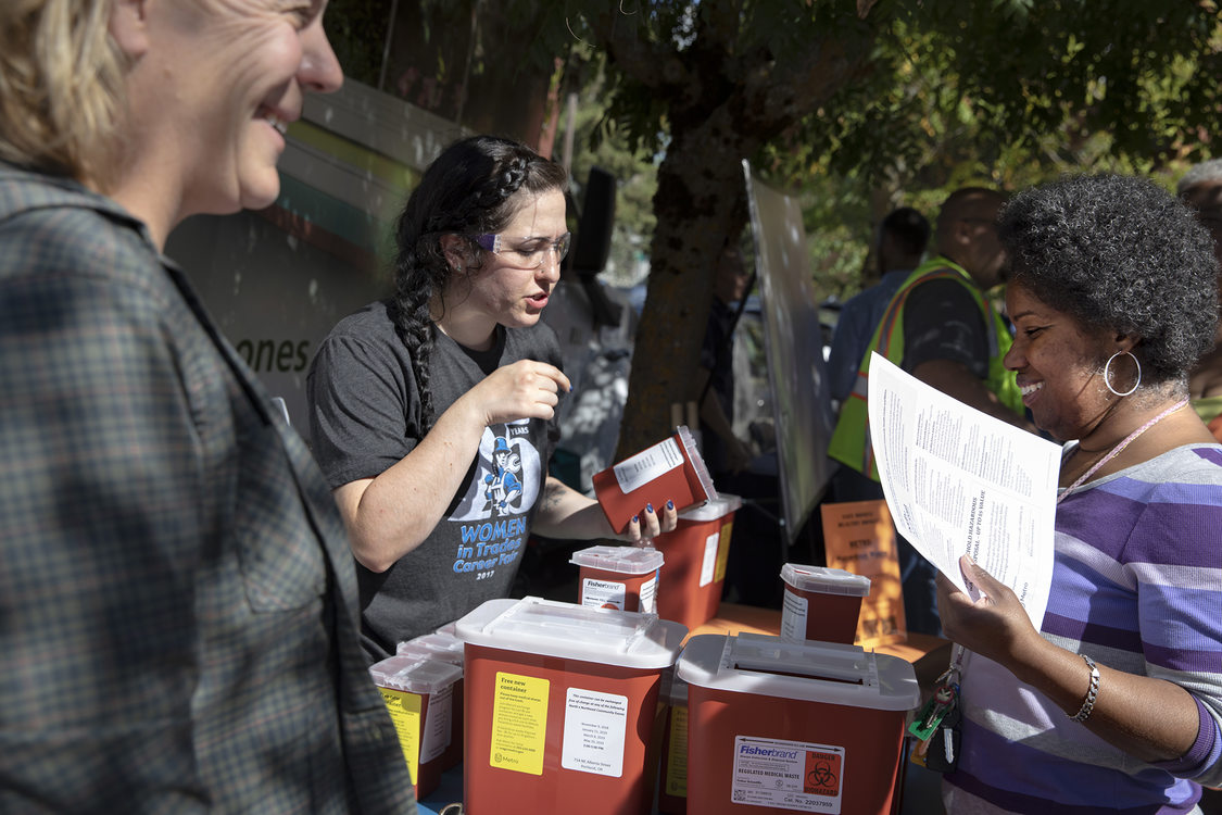 Three people gather around a table full of red medical sharps disposal boxes