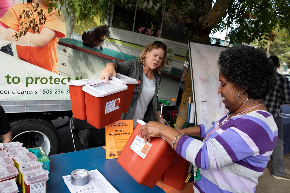 Two people stand over a table where they pick up red sharps disposal boxes