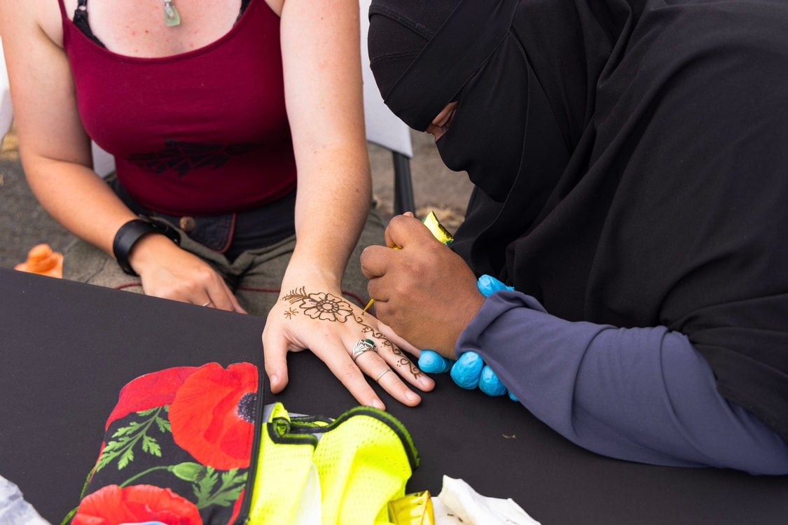 A woman wearing a black niqab applies an intricate floral henna design to a woman’s hand.