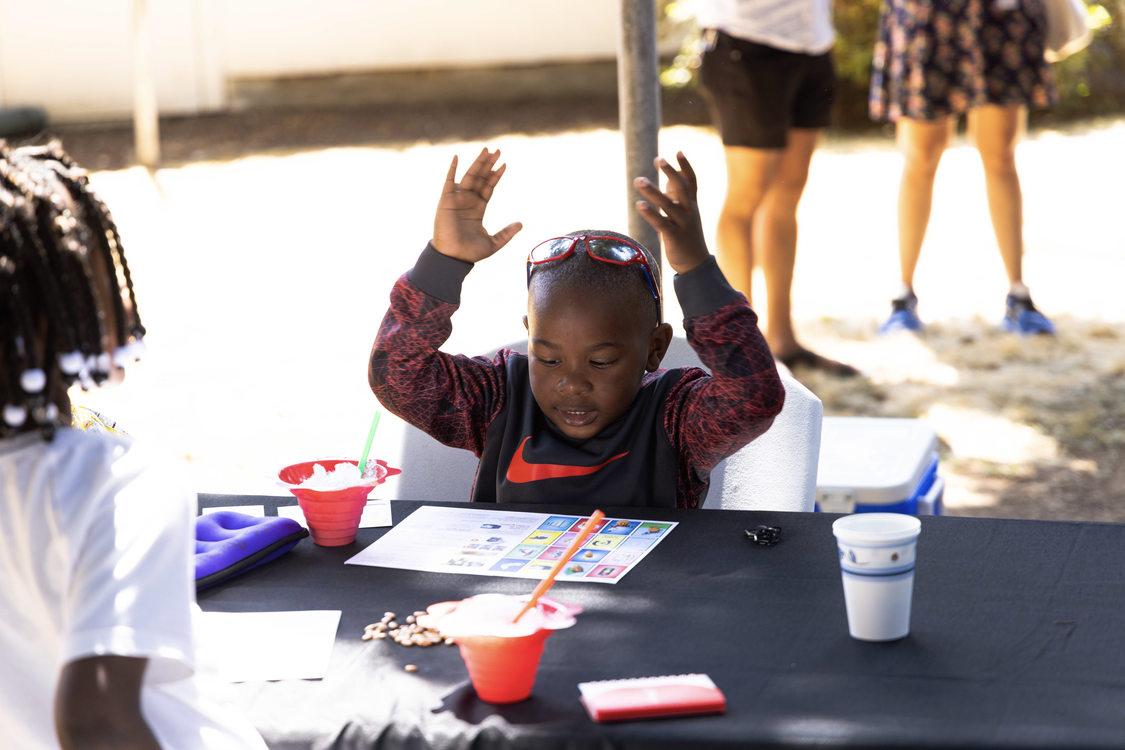 Two young brown skinned children play a game at a table next to two bowls of shaved ice.