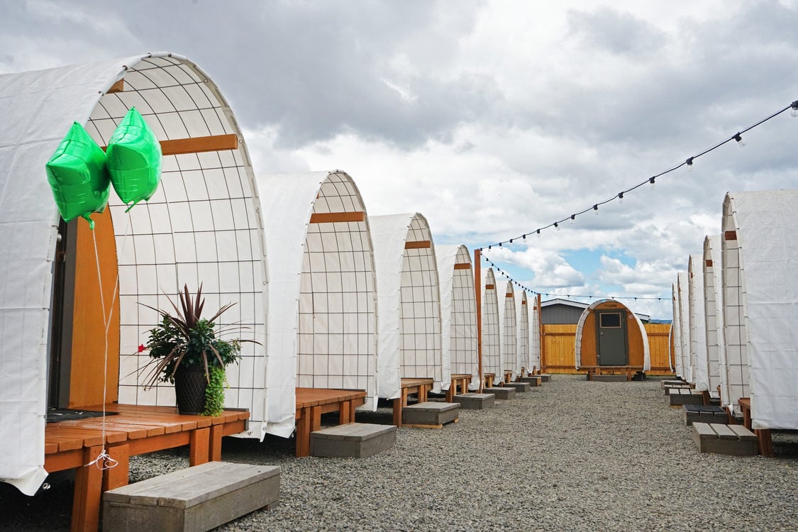 Row of structures with curved white roofs and wooden porches on a gravel lot. 