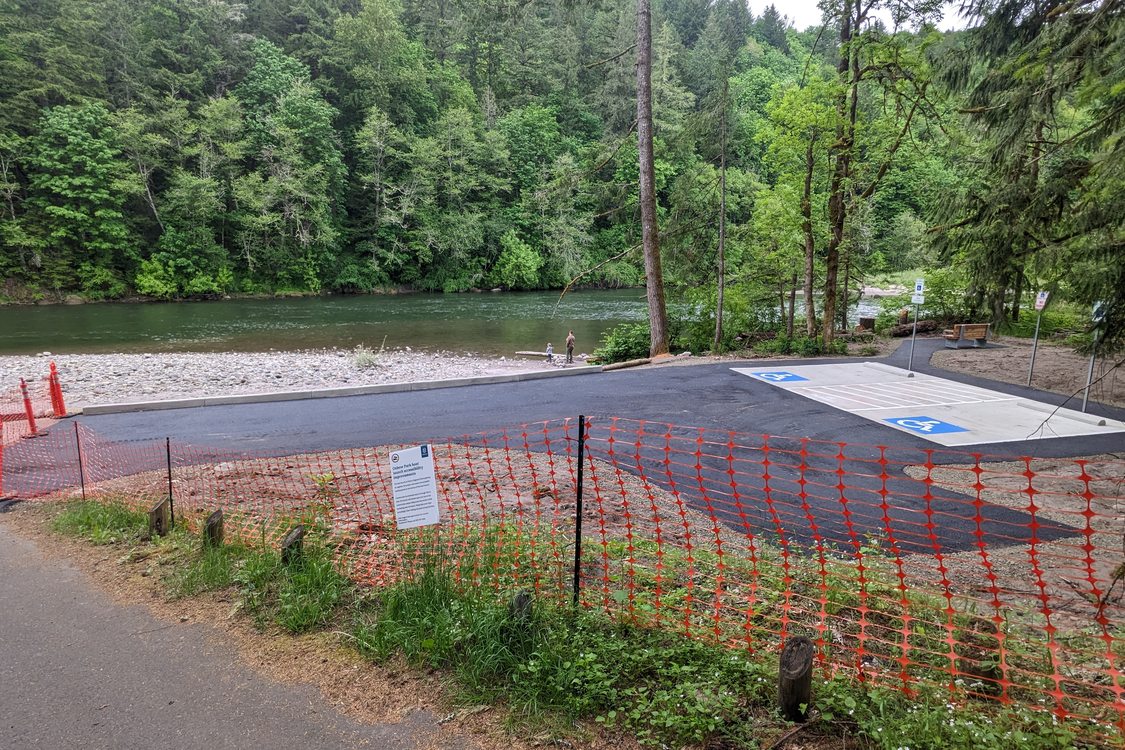 A new ADA parking location under construction in Oxbow Regional Park. The fresh asphalt is temporarily barricaded by an orange construction fence net.