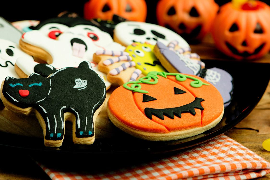 A plate of Halloween themed frosted sugar cookies, including a black cat, a pumpkin and ghosts