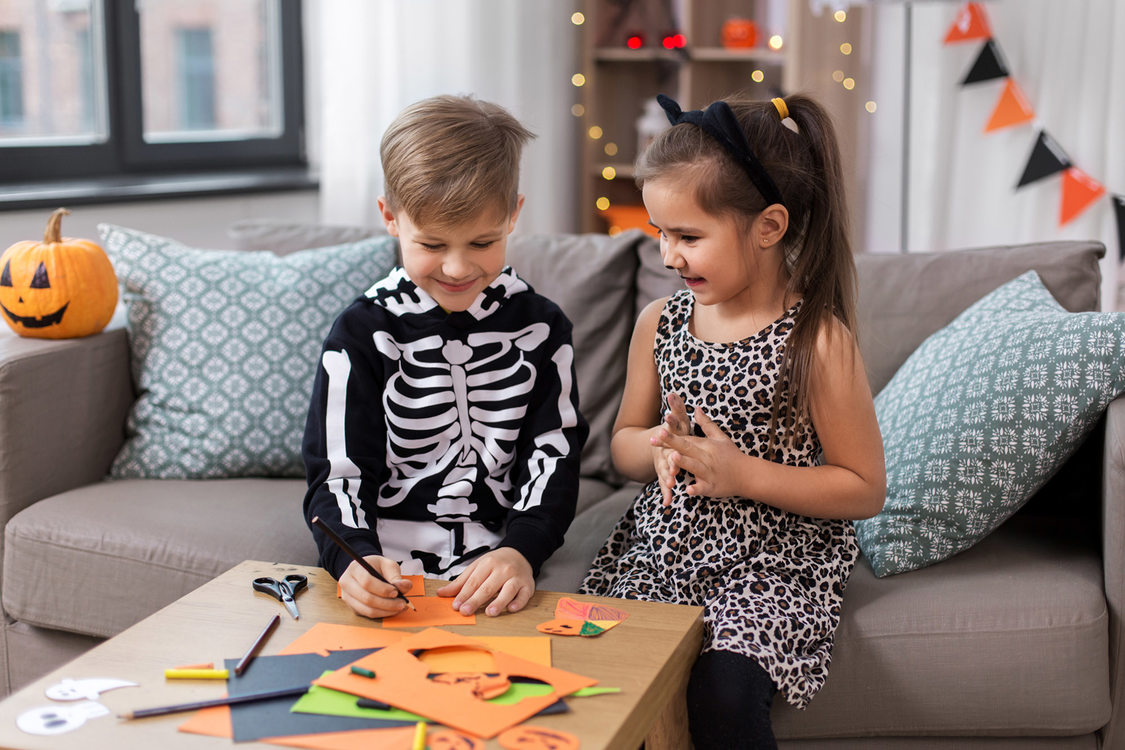 A boy and girl in Halloween outfits create decorations out of construction paper.