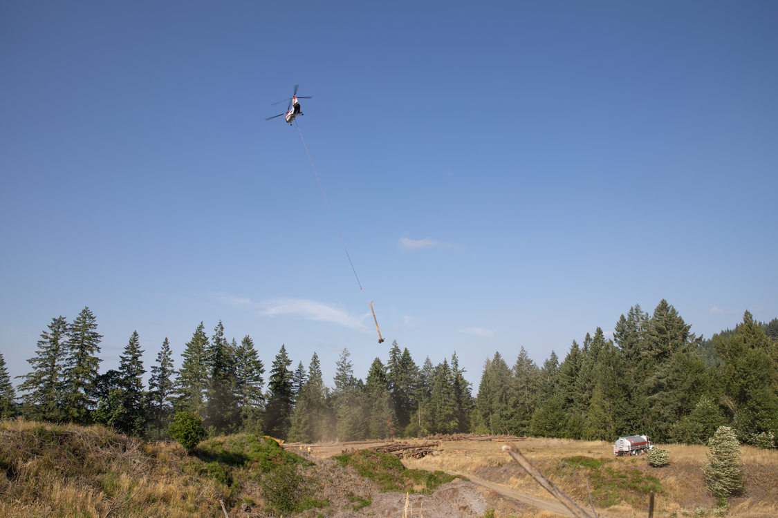 A helicopter carries a log across a wooded landscape. 