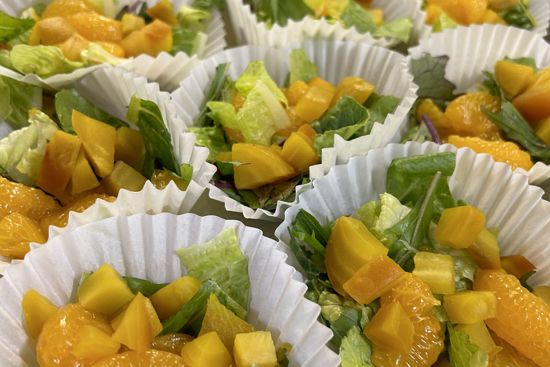 A tray full of small colorful salads in cups, comprised of golden beets, mandarin orange slices, and lettuce.