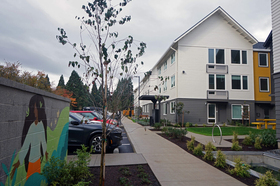 Sidewalk with a mural on the left side and multifamily residential buildings on the right side.