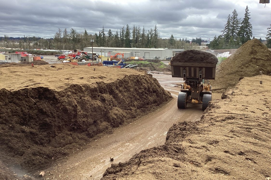 Image of bulldozer transporting compost among large mounds of additional composting material at Grimm's Fuel Company, Inc..  