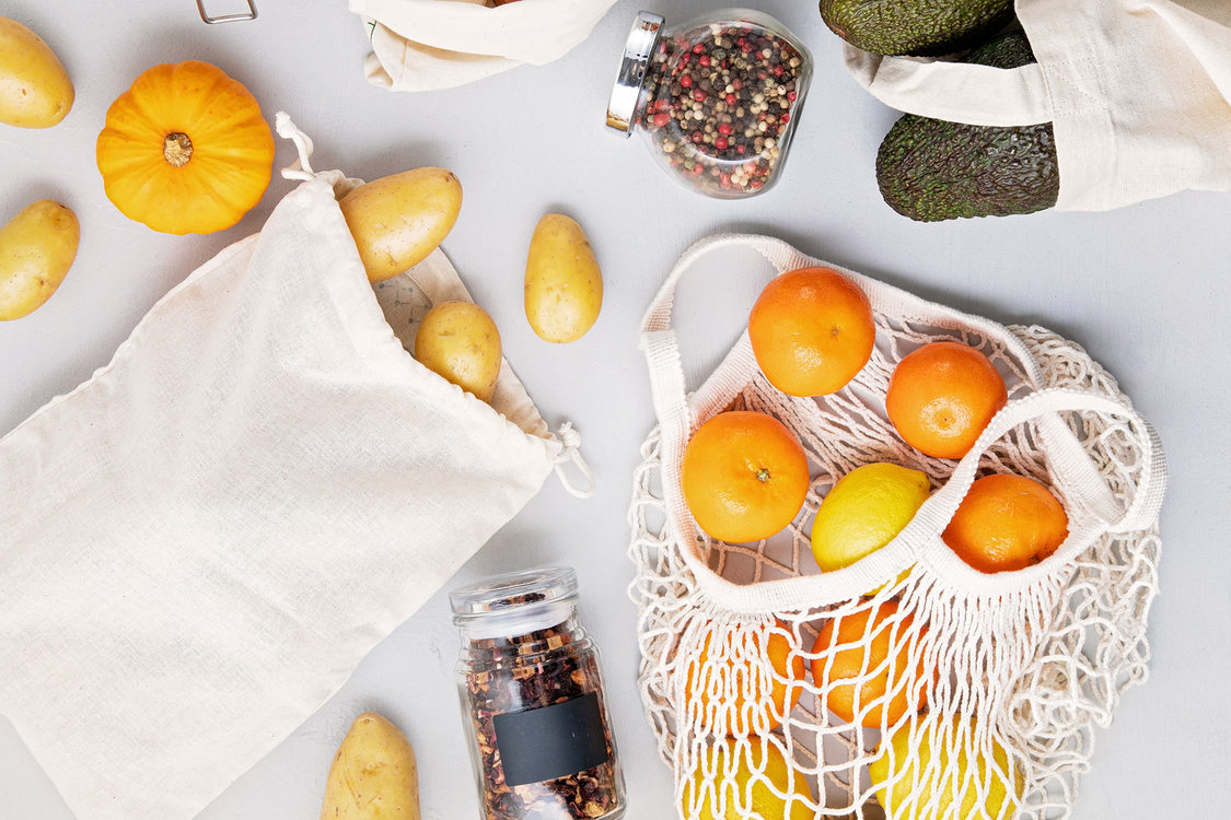 reusable bags with potatoes and oranges tumbling out onto a table