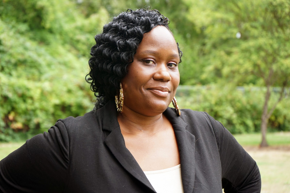 Woman wearing a black blazer posing in a park setting.