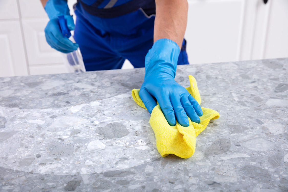 A man wearing blue gloves cleans a grey stone countertop