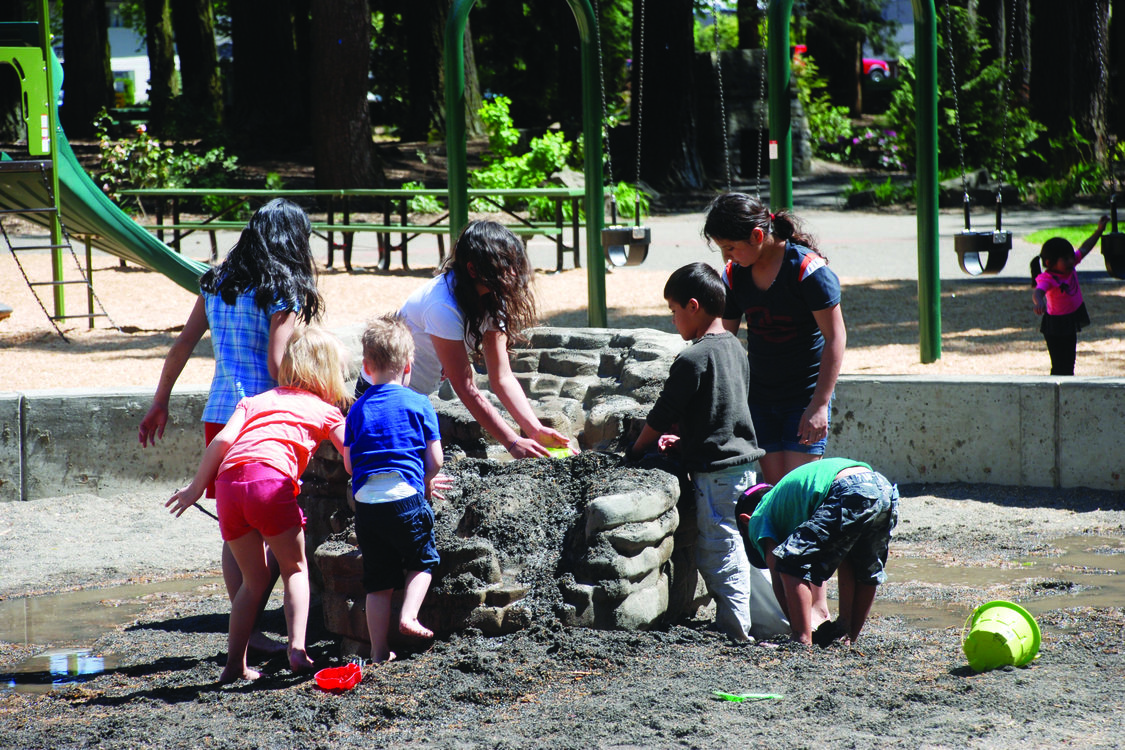 A group of children play with water and sand at a play table at a park. 