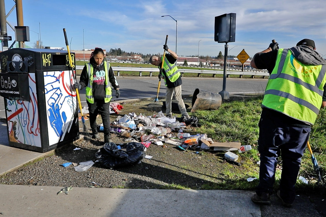 Three employees of Cultivate Initiatives Community Beautification crew raking trash by a freeway.