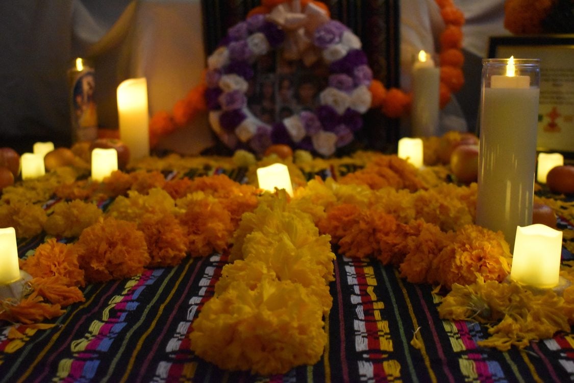 An alter created for ancestors for Dia de los Muertos with lit candles, colorful flowers and a patterned cloth