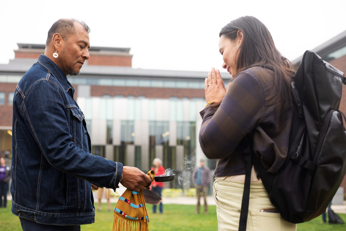 An indigenous person performs a smudging ceremony for another person who holds their hands in a praying position