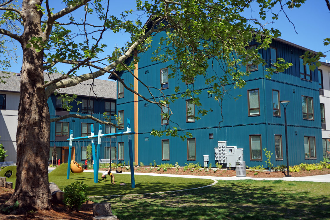 Grassy plaza between multifamily housing buildings with a swingset in the middle.