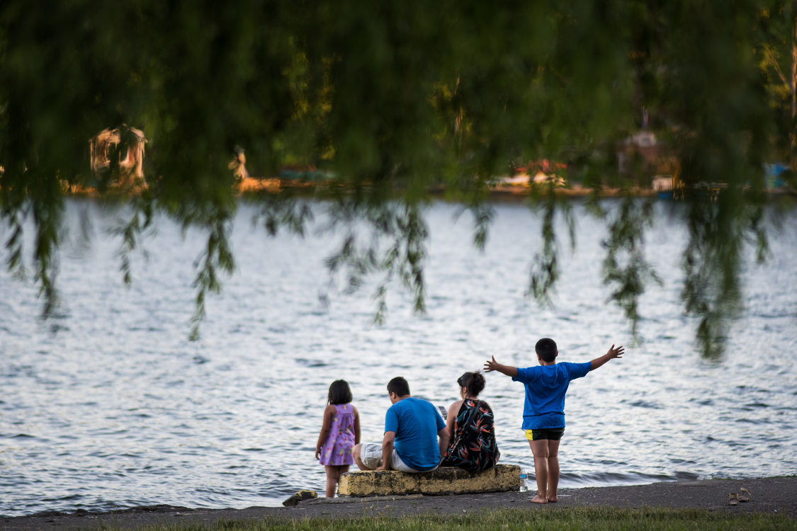 four people -- two adults and two children -- seen from behind facing Blue Lake. The adults are seated, while the children stand, one of them with their arms outstretched.