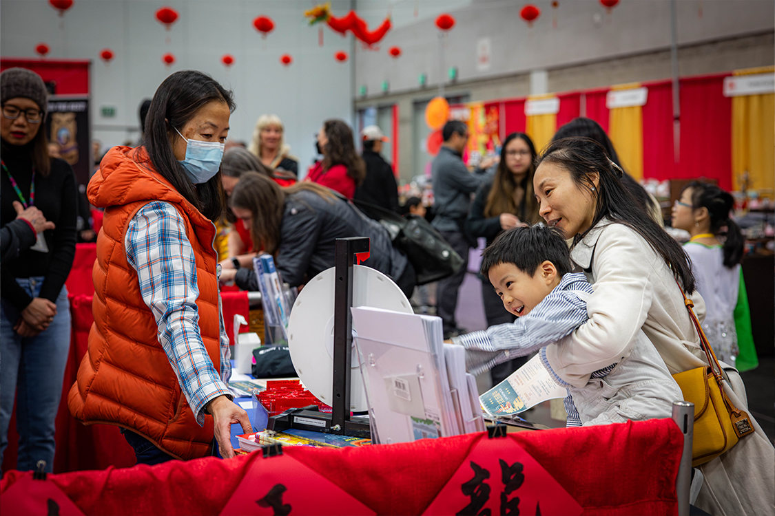 A woman holds a child reaching for a spinning game wheel on a display table for the Chinese New Year in the Oregon Convention Center.
