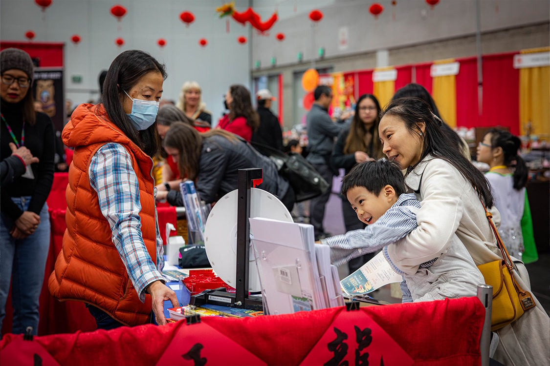 A woman holds a child reaching for a spinning game wheel on a display table for the Chinese New Year in the Oregon Convention Center.