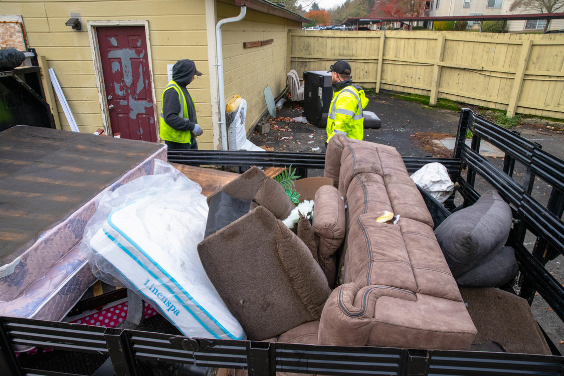 Overhead view of full trailer hall with couches and other furniture while waste management haulers collect more discarded items in an apartment complex.