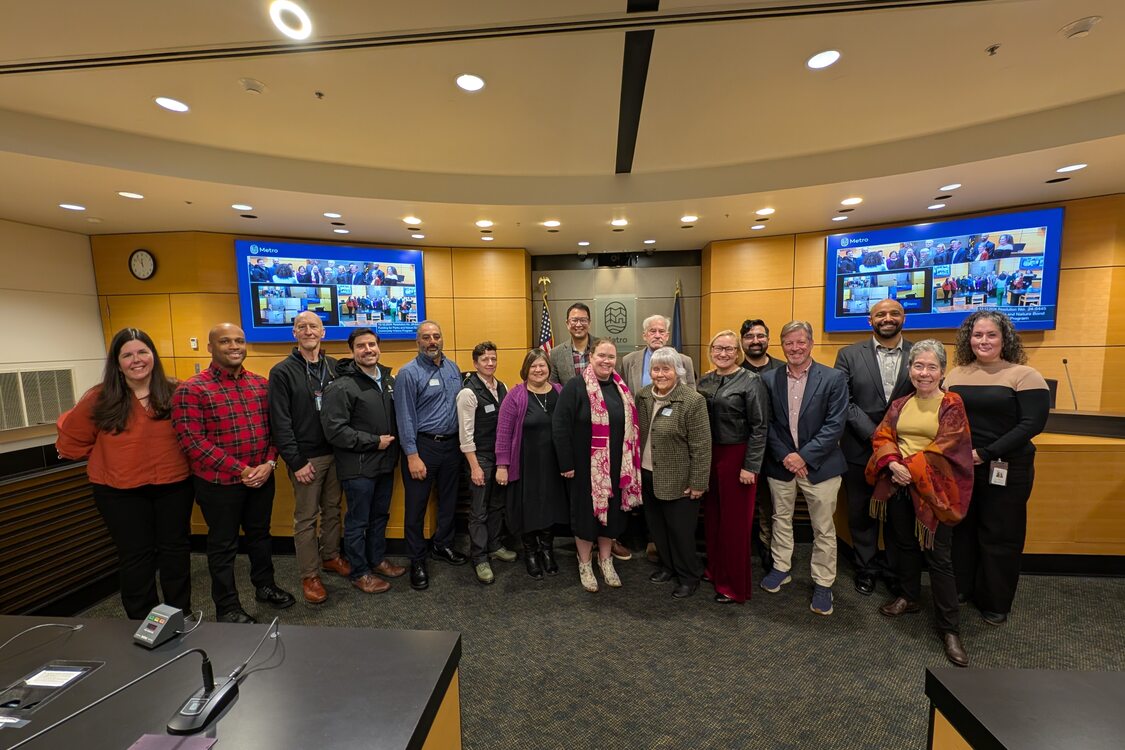 A group of people pose in front of a council chambers.