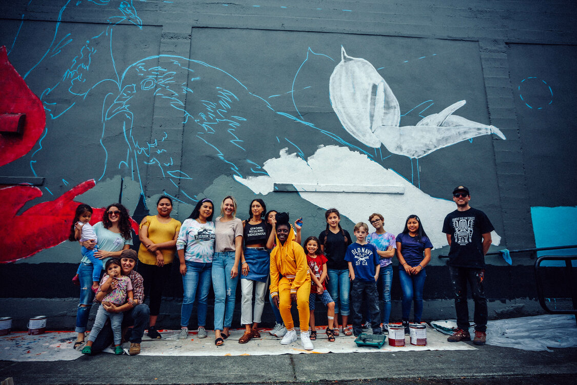 A group of people pose in front of a mural.
