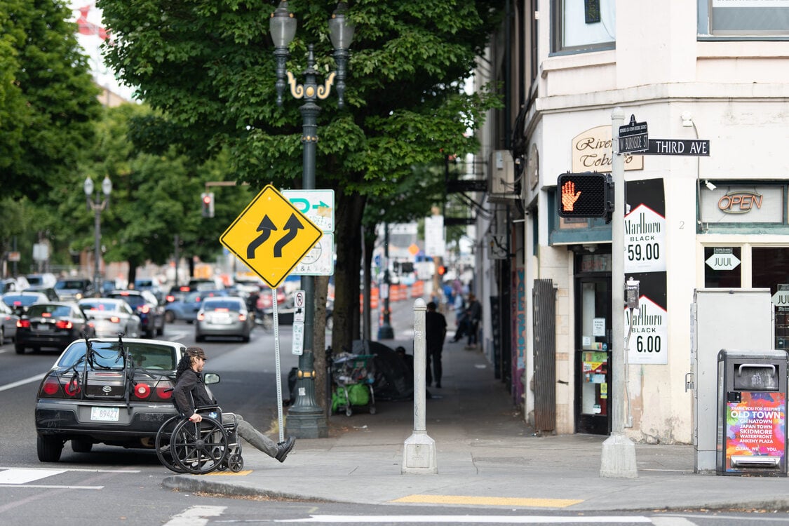 A person in a wheelchair crosses the street onto a sidewalk using a curb ramp