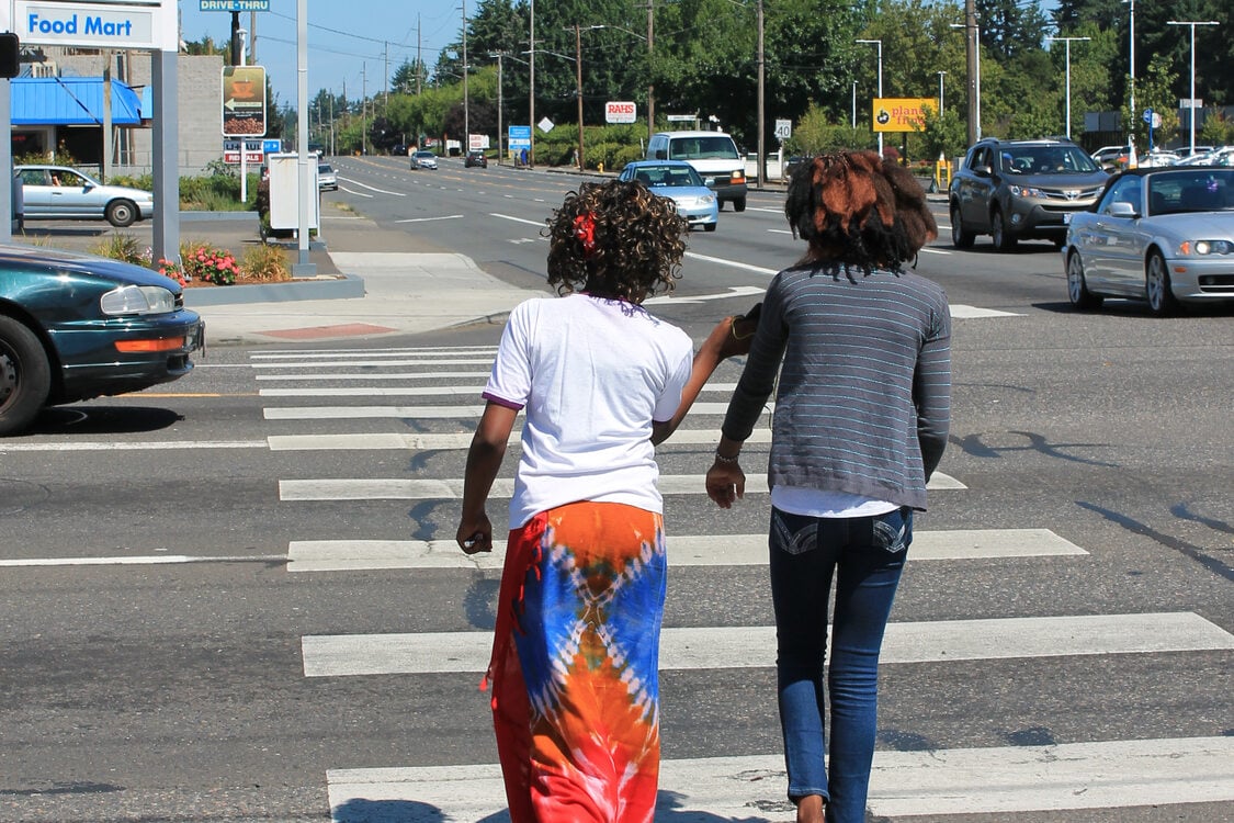 Two black women walk along a crosswalk on a busy road