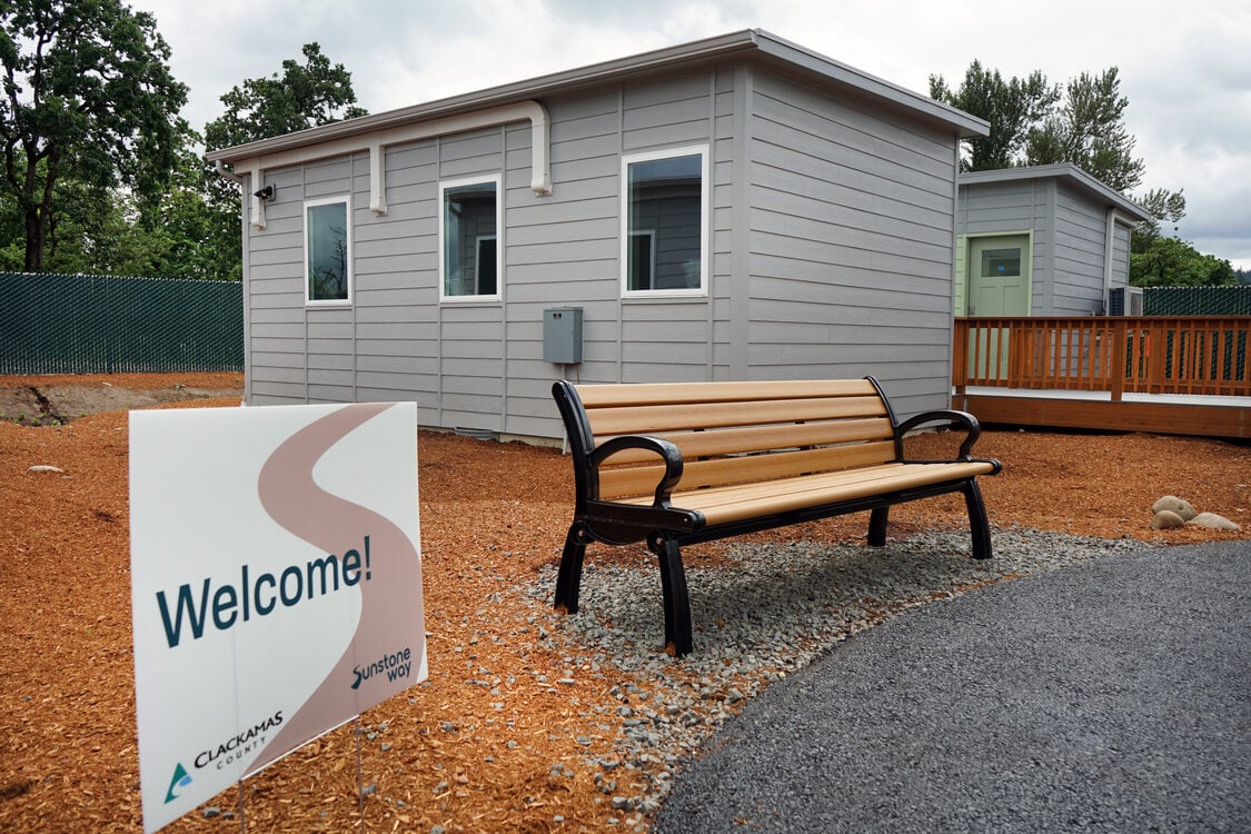 Bench in front of a grey bungalow, with a Welcome sign next to it. 