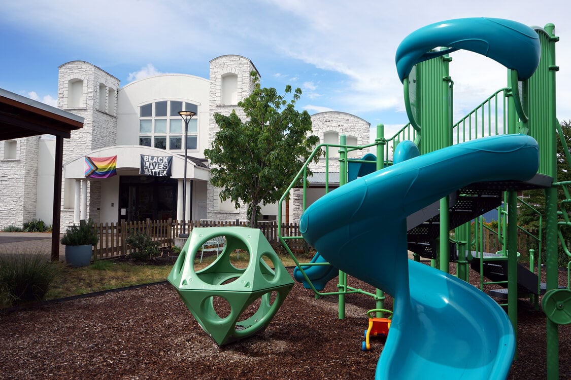 Blue and green playground in the foreground, with white multi-story building in the background. 