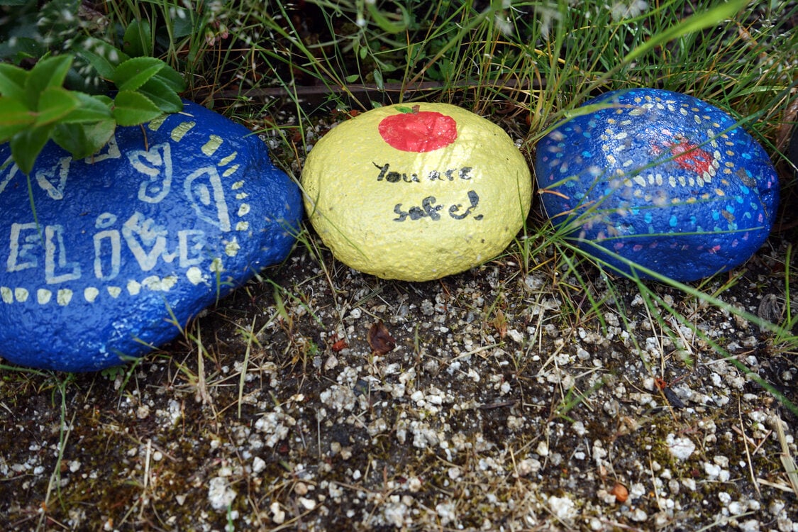 Painted stones in blue and yellow. Middle stone reads “you are safe.”