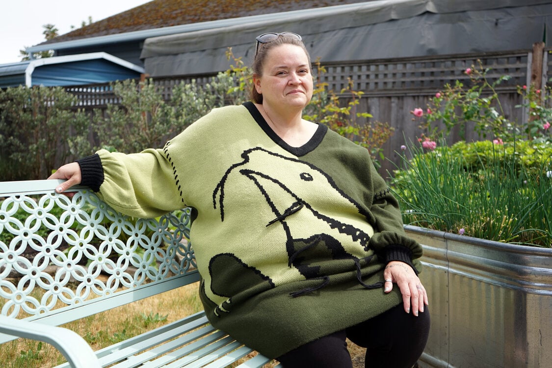Woman in a green sweater with a dinosaur design sitting on a metal bench. 