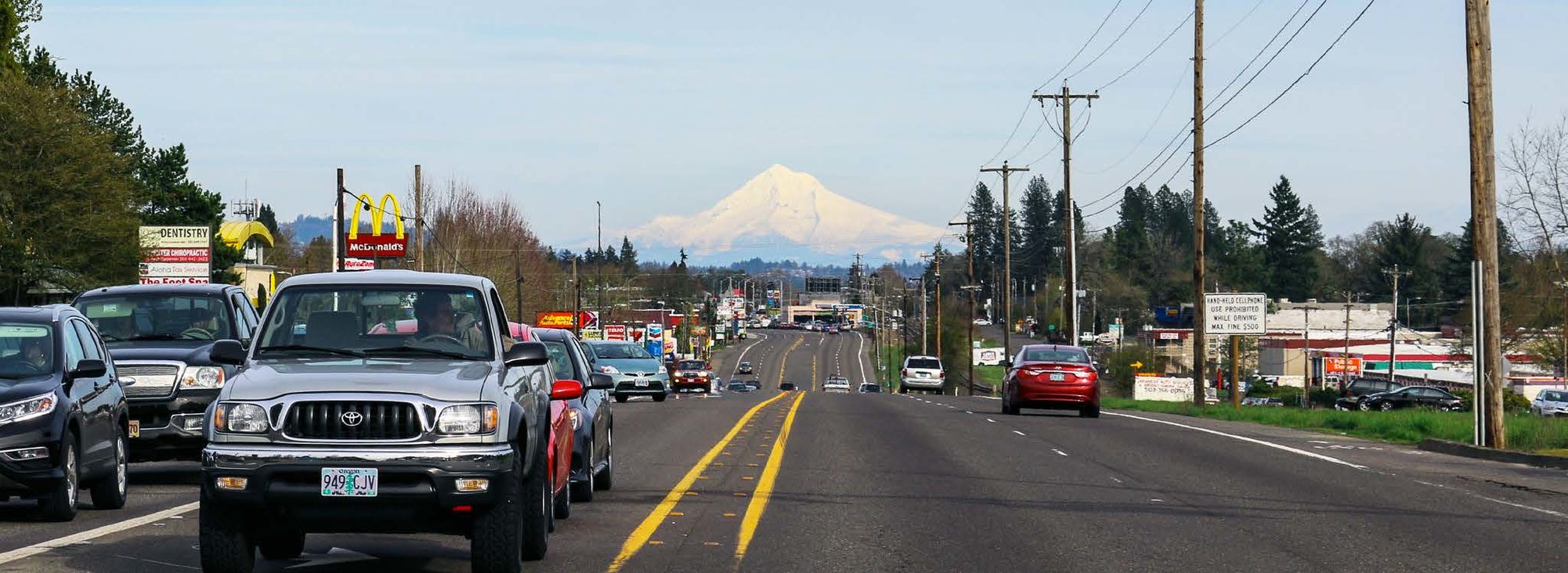 A view of Southwest Tualatin Valley Highway looking east, with a snow-covered Mount Hood in the distance and heavy traffic on the road.